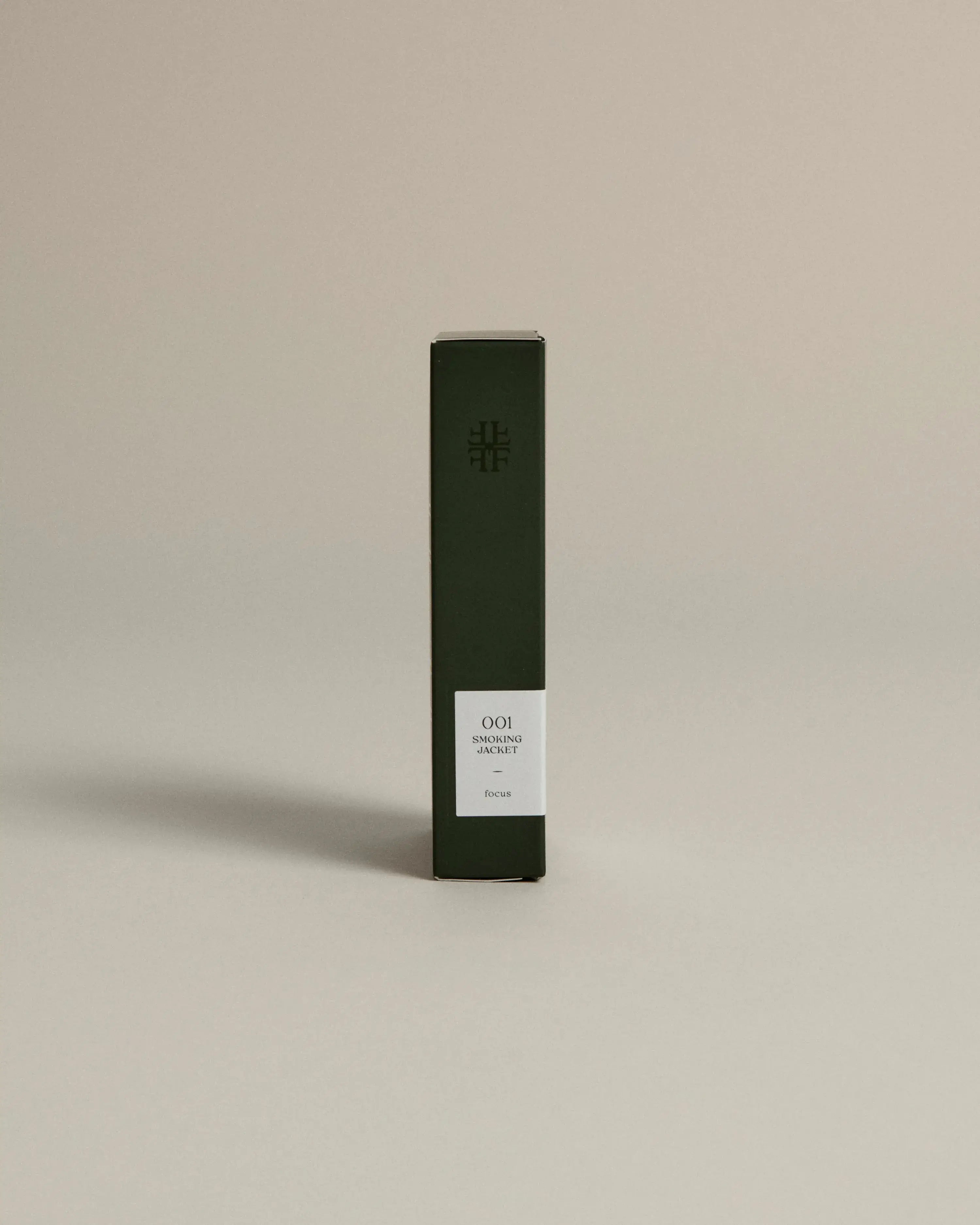 Minimalist dark green box labeled ‘001 Smoking Jacket – Focus’ by FORGRAVE, standing upright on a beige background.