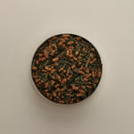 Overhead view of loose herbal tea blend in a round tin, featuring dried tea leaves on a beige background.