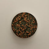 Overhead view of loose herbal tea blend in a round tin, featuring dried tea leaves on a beige background.