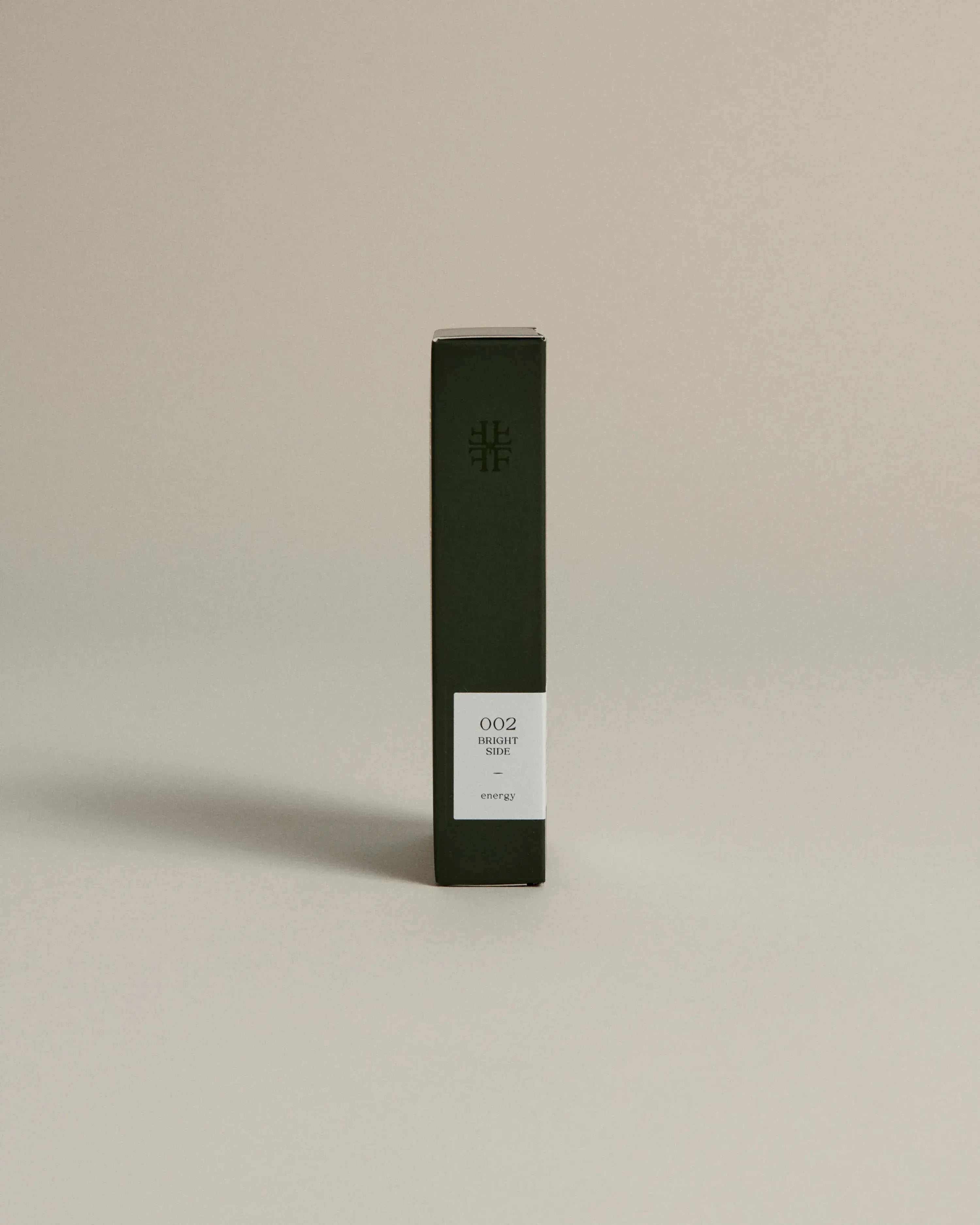 Minimalist dark green box labeled ‘002 Bright Side – Energy’ by FORGRAVE, standing upright on a beige background.