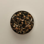 Overhead view of loose herbal tea blend in a round tin, featuring dried tea leaves beige background.