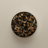 Overhead view of loose herbal tea blend in a round tin, featuring dried tea leaves beige background.