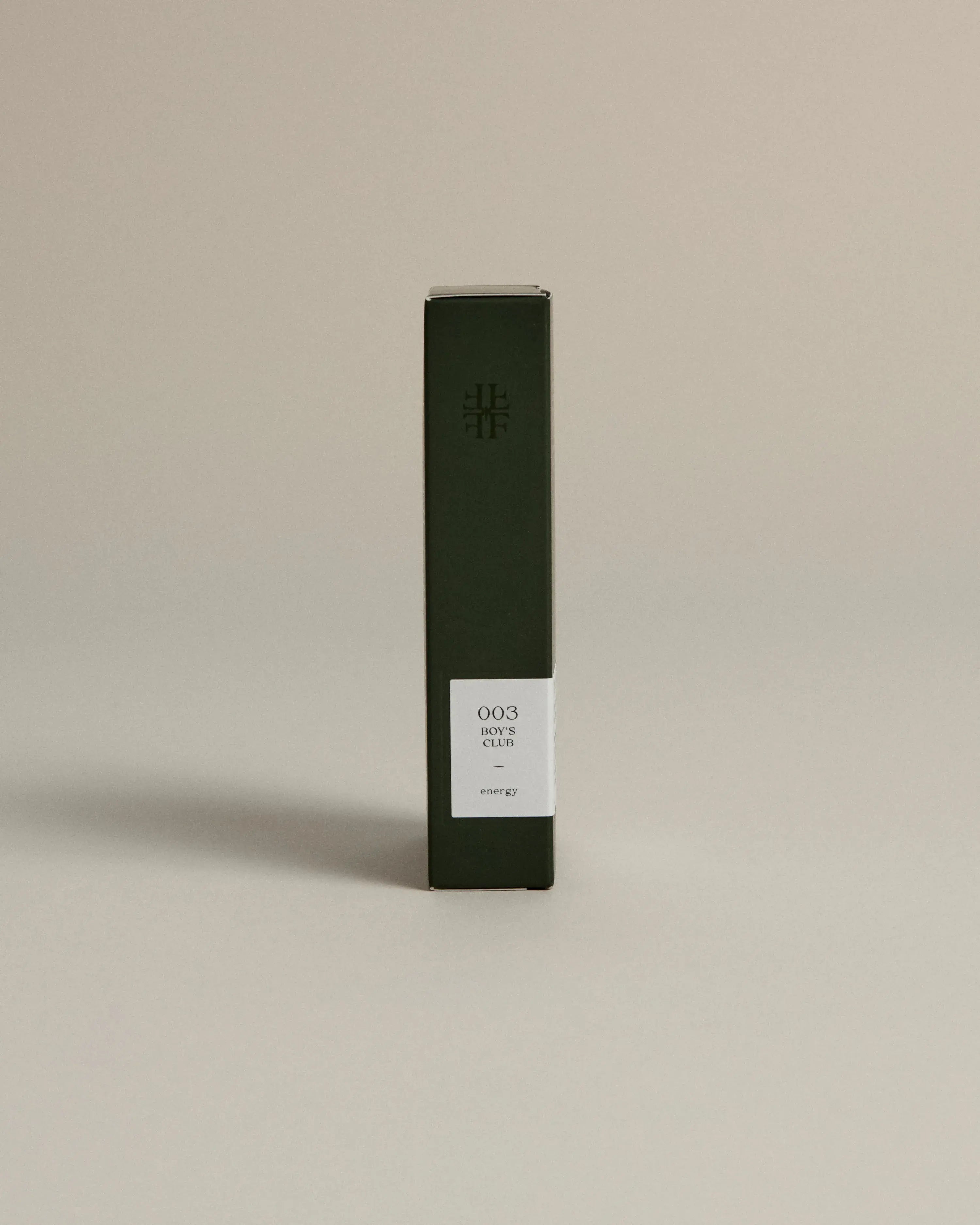 Minimalist dark green box labeled ‘003 Boy's Club– Energy’ by FORGRAVE, standing upright on a beige background.