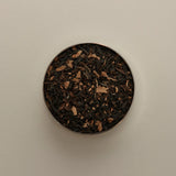Overhead view of loose herbal tea blend in a round tin, featuring dried tea leaves on a beige background.