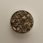 Overhead view of loose herbal tea blend in a round tin, featuring dried tea leaves on a beige background.