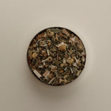 Overhead view of loose herbal tea blend in a round tin, featuring dried tea leaves on a beige background.