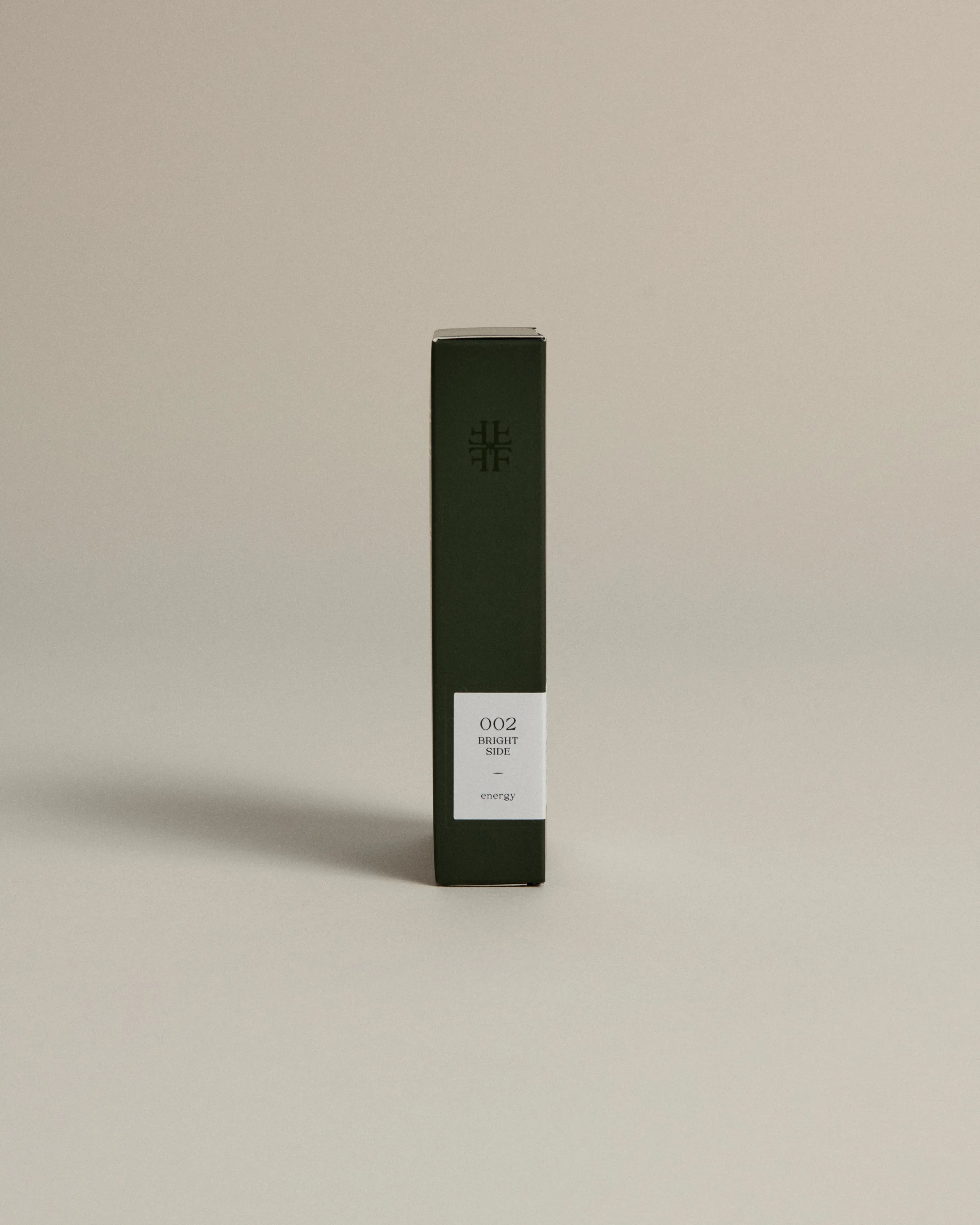 Minimalist dark green box labeled ‘002 Bright Side – Energy’ by FORGRAVE, standing upright on a beige background.