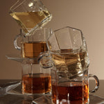 Stacked clear glass mugs filled with various shades of tea, reflecting warm light on a beige background.