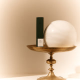Dark green FORGRAVE ‘001 Smoking Jacket – Focus’ tea box displayed on a brass pedestal with a white marble orb beside it.