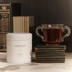 FORGRAVE ‘Bright Side’ tea tin beside a glass cup of tea resting on stacked vintage books, styled on a marble surface.