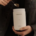 Person in black jacket scooping tea from a white ‘FORGRAVE 005 Mint Mantra white blend’ canister.