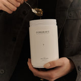 Person in black jacket scooping tea from a white ‘FORGRAVE 005 Mint Mantra white blend’ canister.