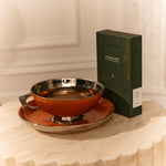 A green Forgrave tea box labeled "003 Boys' Club" sits beside a metallic orange teacup and saucer on a textured beige table.