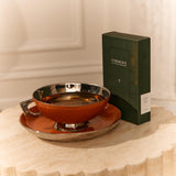 A green Forgrave tea box labeled "003 Boys' Club" sits beside a metallic orange teacup and saucer on a textured beige table.