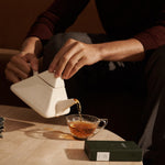 Person pours tea from a modern white teapot into a glass mug, with a FORGRAVE ‘Bright Side’ box on a stone table nearby.