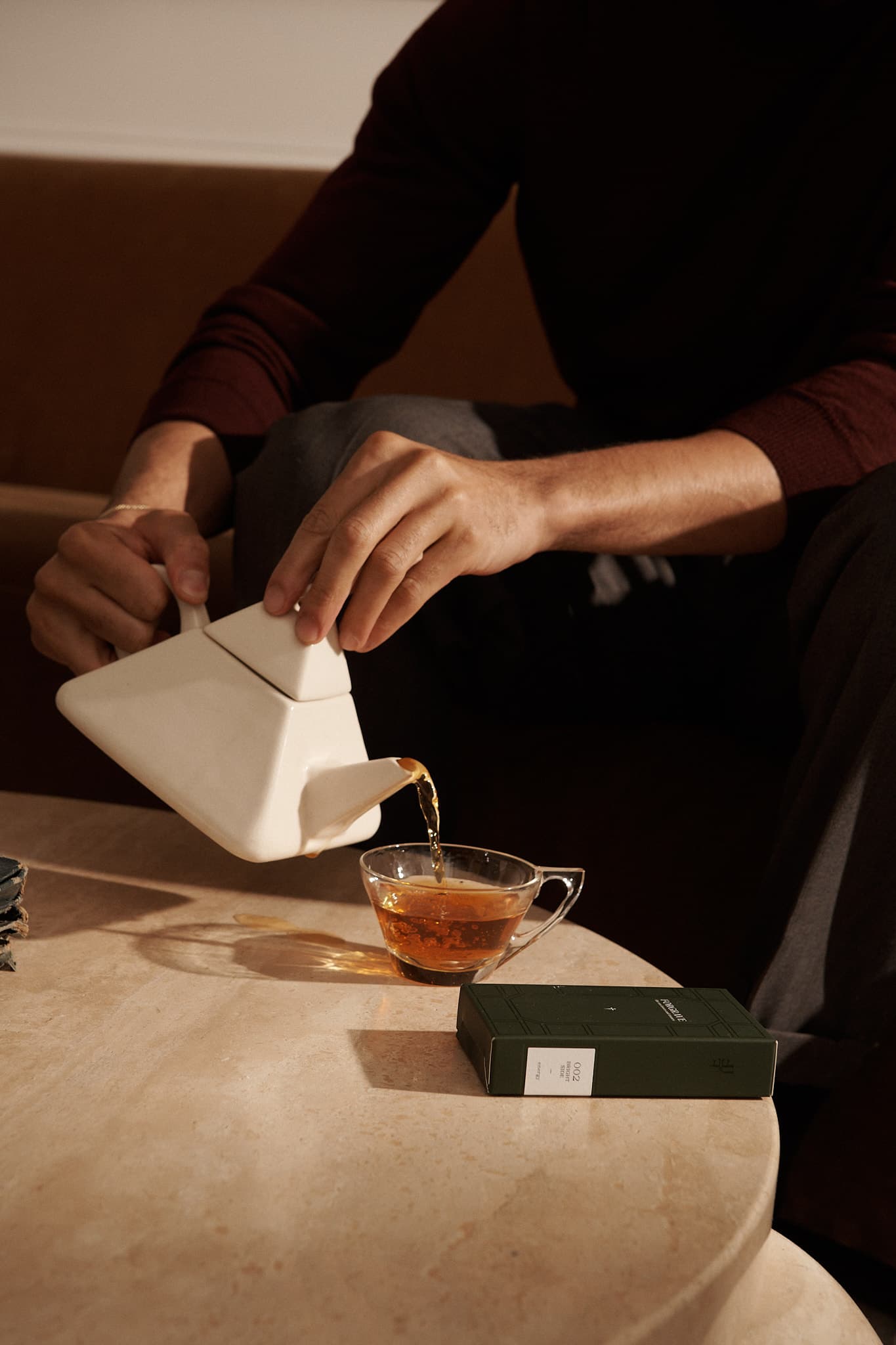 Person pours tea from a modern white teapot into a glass mug, with a FORGRAVE ‘Bright Side’ box on a stone table nearby.