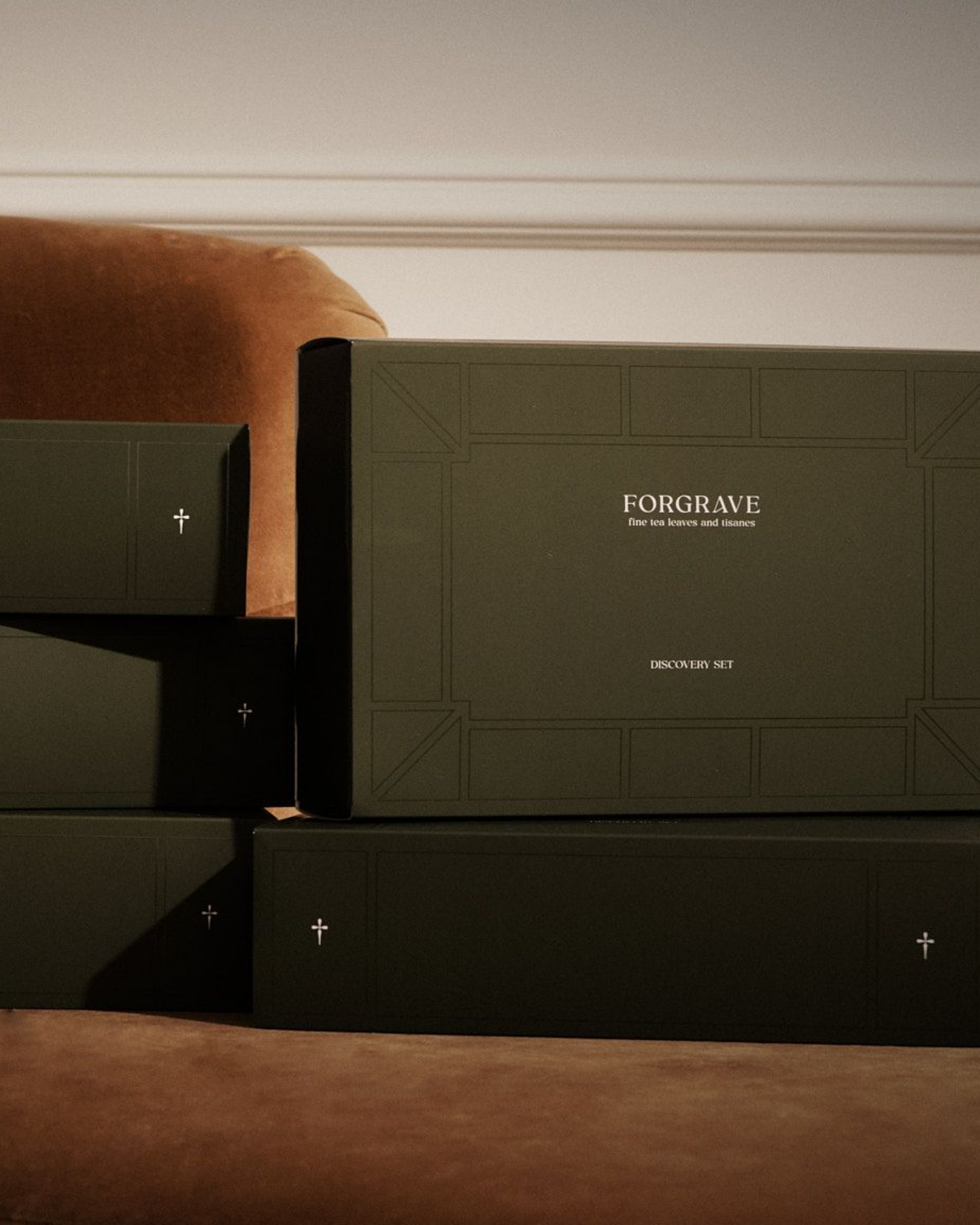 Minimalist dark green ‘FORGRAVE Discovery Set’ boxes with fine tea branding. Stacked on a brown couch.