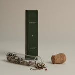 Dark green box labeled ‘FORGRAVE The Glass Cigar’ next to a cork and a glass tube spilling loose tea leaves with floral accents.